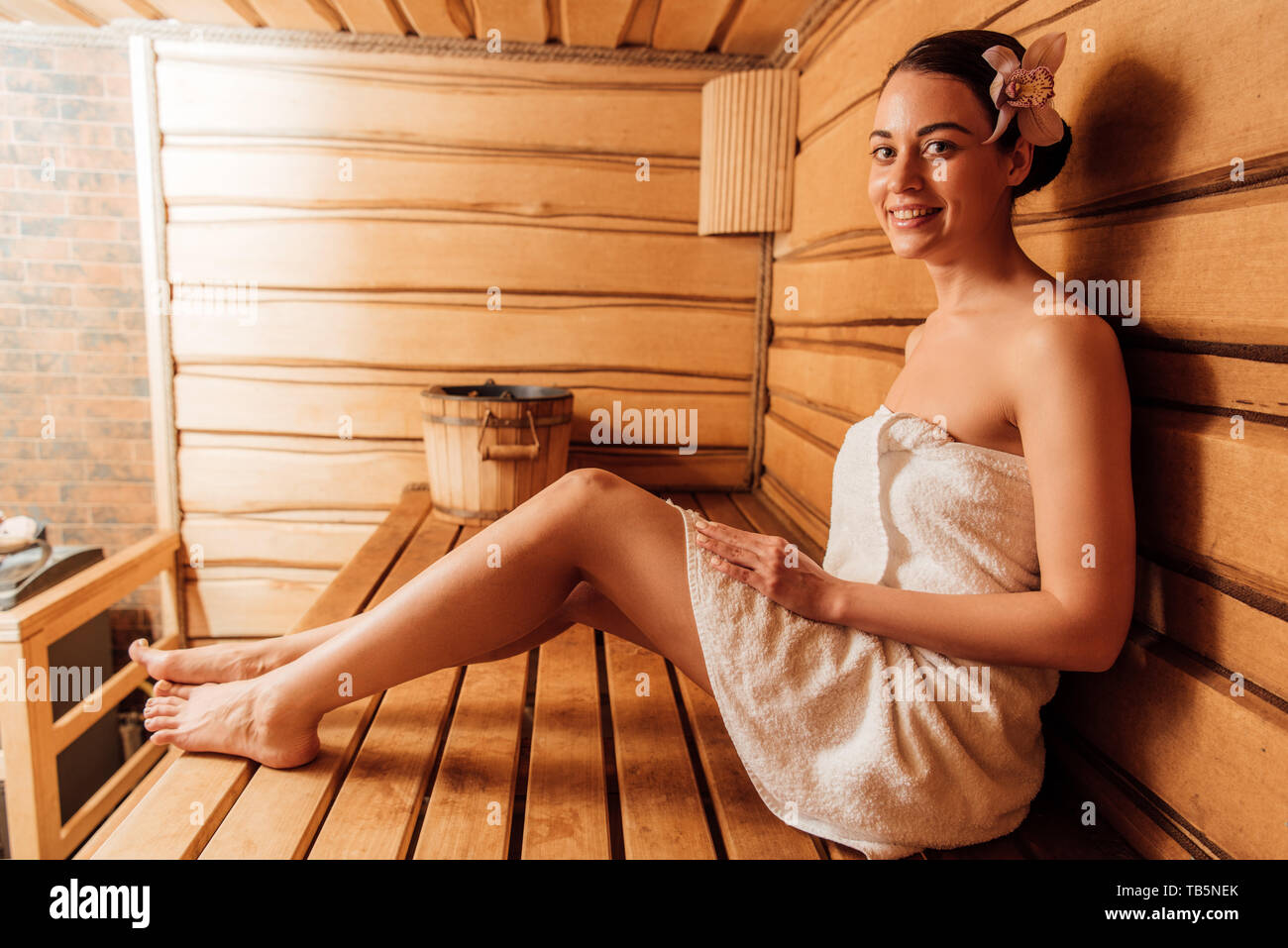 smiling woman in towel with flower in hair in sauna Stock Photo