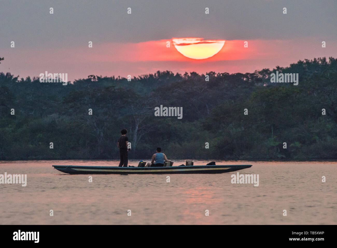 The sun sets over Cuyabeno Wildlife Reserve in Amazonian Ecuador and local people in a boat observe and fish. Stock Photo
