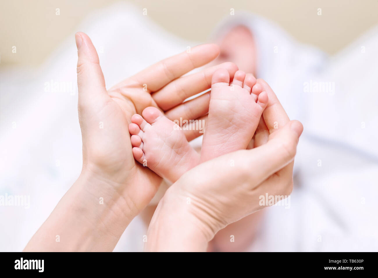 Mother holding newborn baby feet in hands. Mom taking care about infant