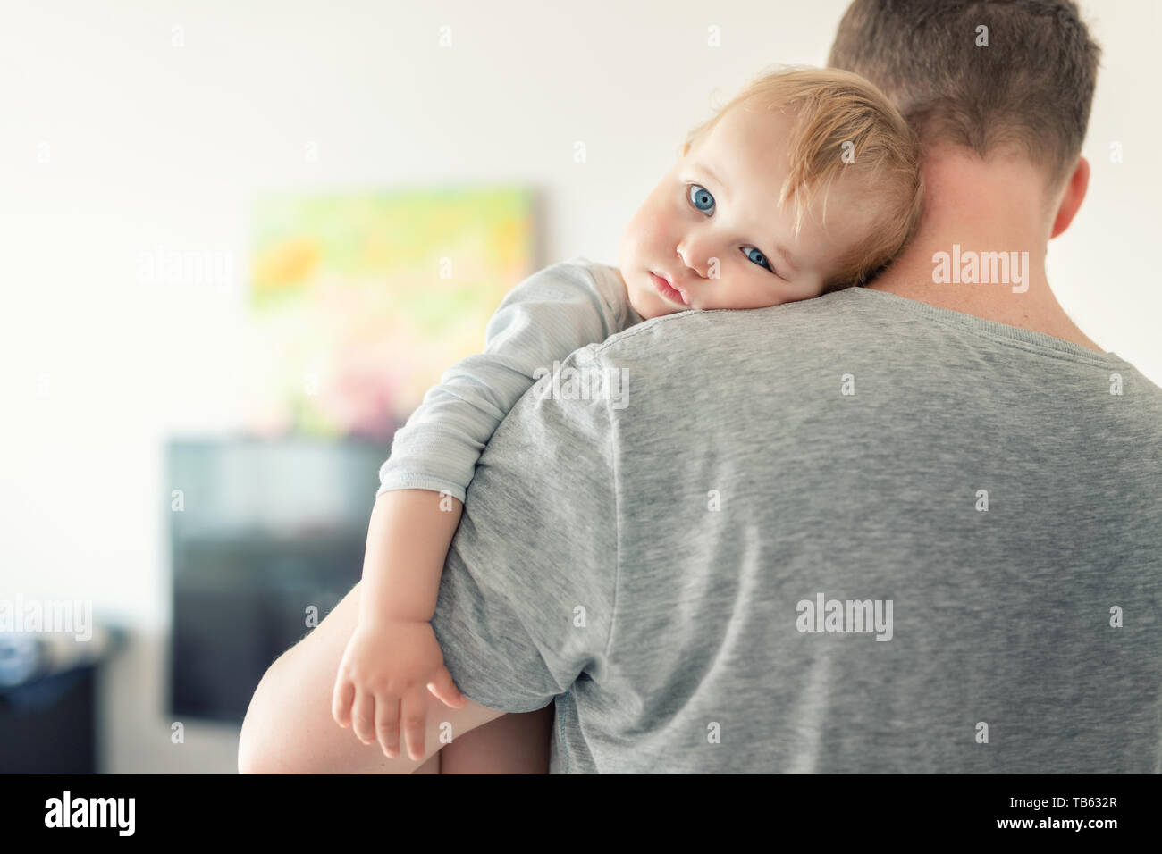 Close-up portrait of cute adorable blond caucasian toddler boy on fathers shoulder indoors. Sweet little child feeling safety on daddys hand Stock Photo