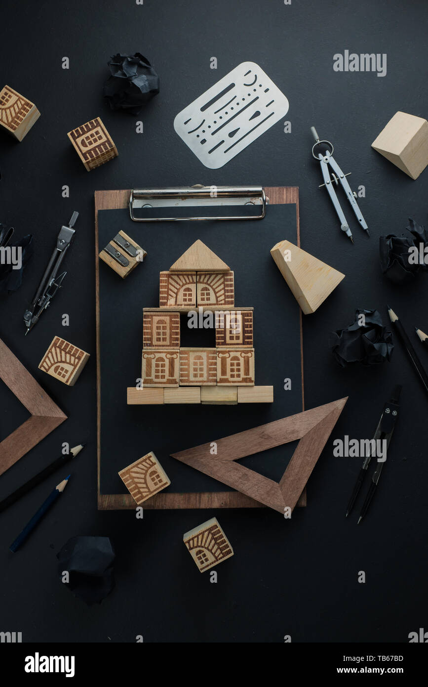 House construction, planning, and repairment concept. Wooden block home on a clipboard with engineering equipment, compasses, rulers and pencils. Stock Photo