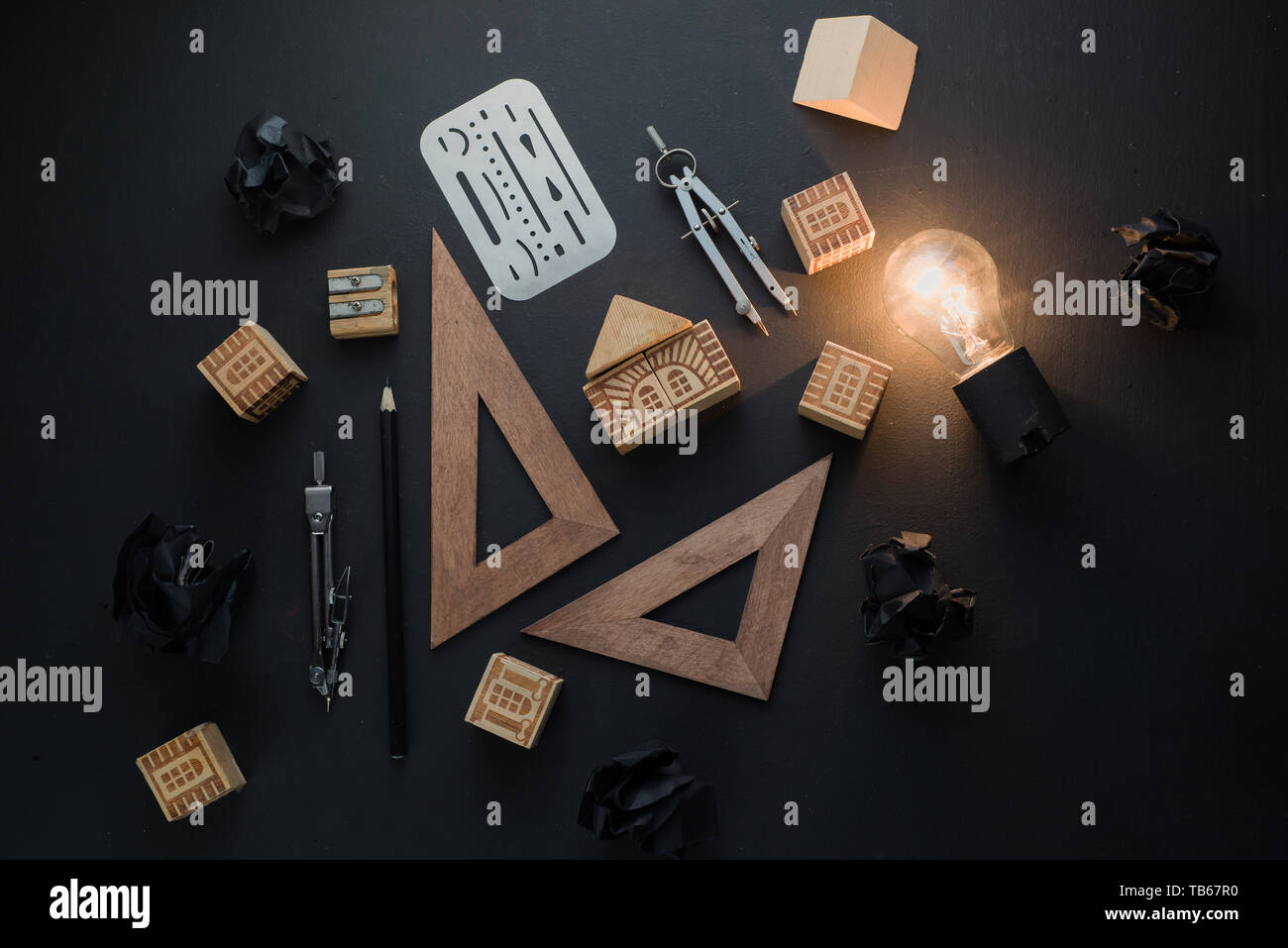 Innovation and creativity concept for engineering and science. Light bulb shining in black on black flat lay with crumpled paper balls and pencils. Stock Photo