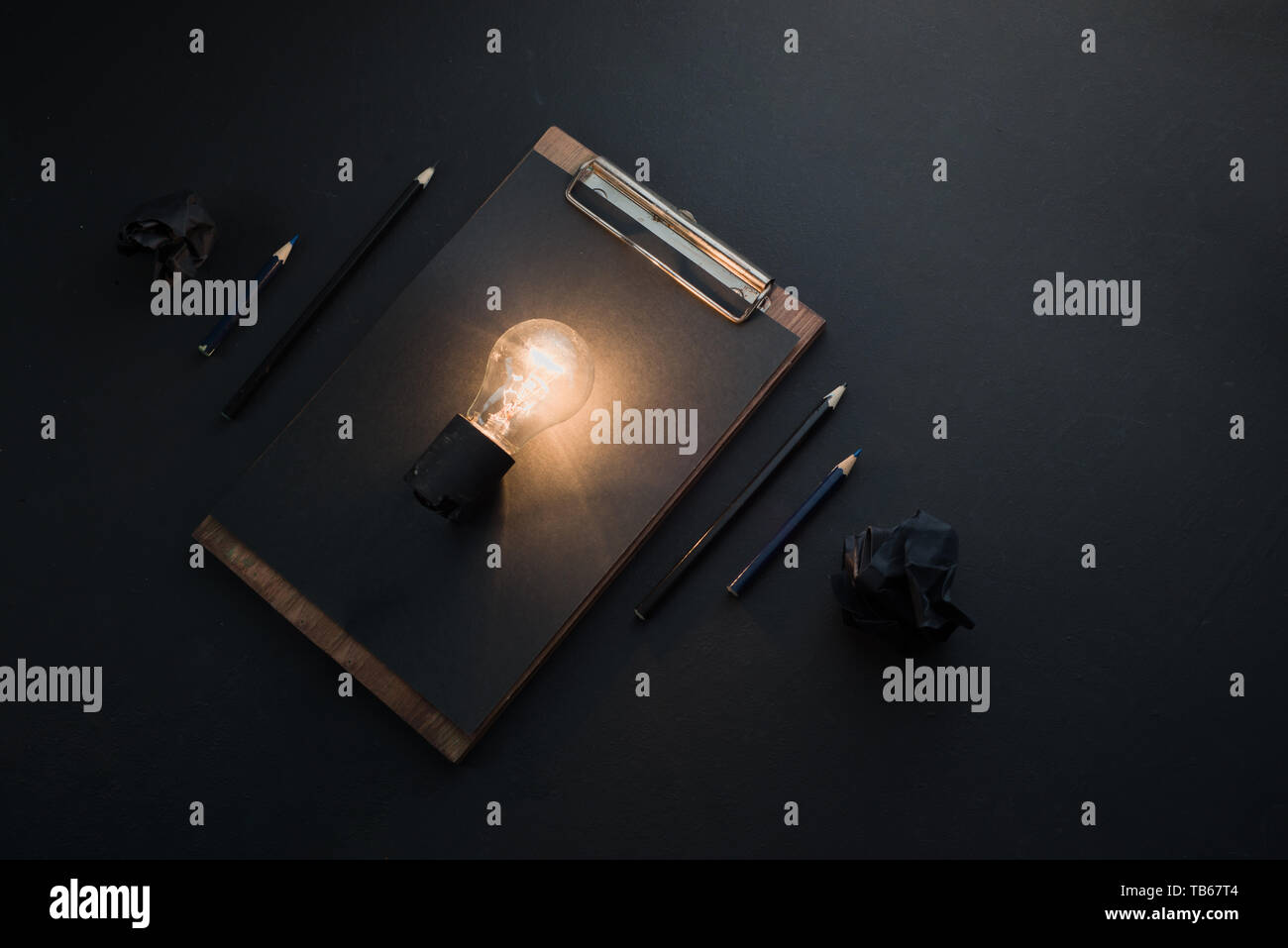 Light bulb shining in black flat lay with crumpled paper balls and a clipboard. The idea for engineering, building or construction concept with copy s Stock Photo