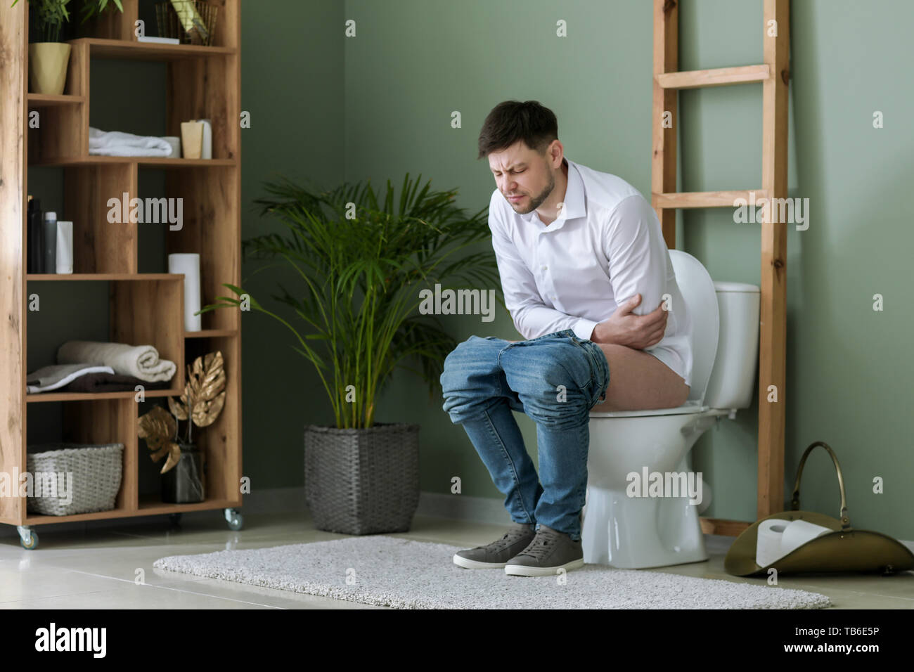 Man suffering from diarrhea while sitting on toilet bowl at home Stock