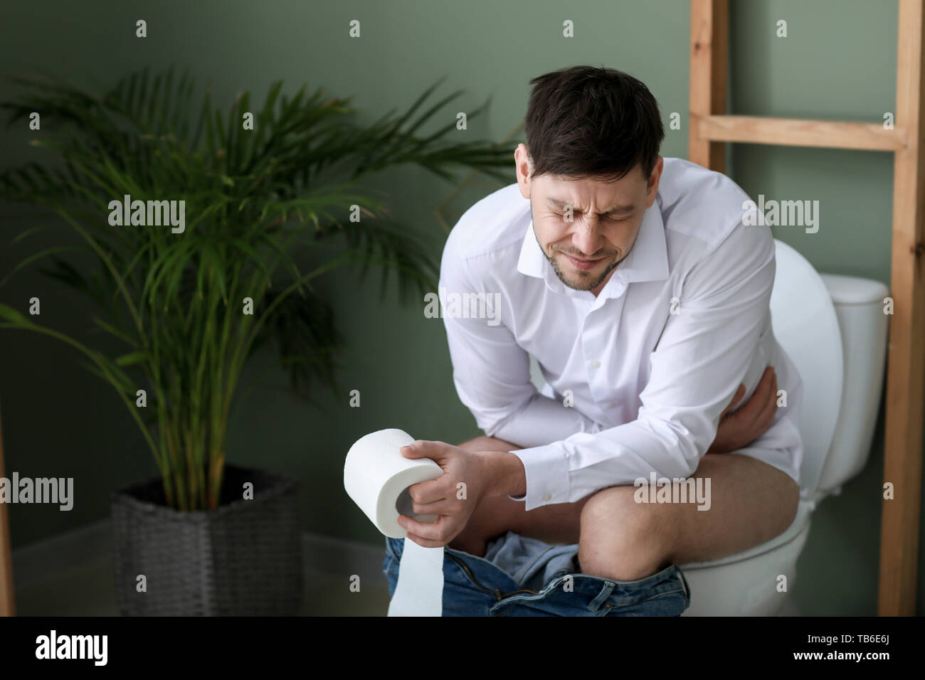 Man suffering from diarrhea while sitting on toilet bowl at home Stock
