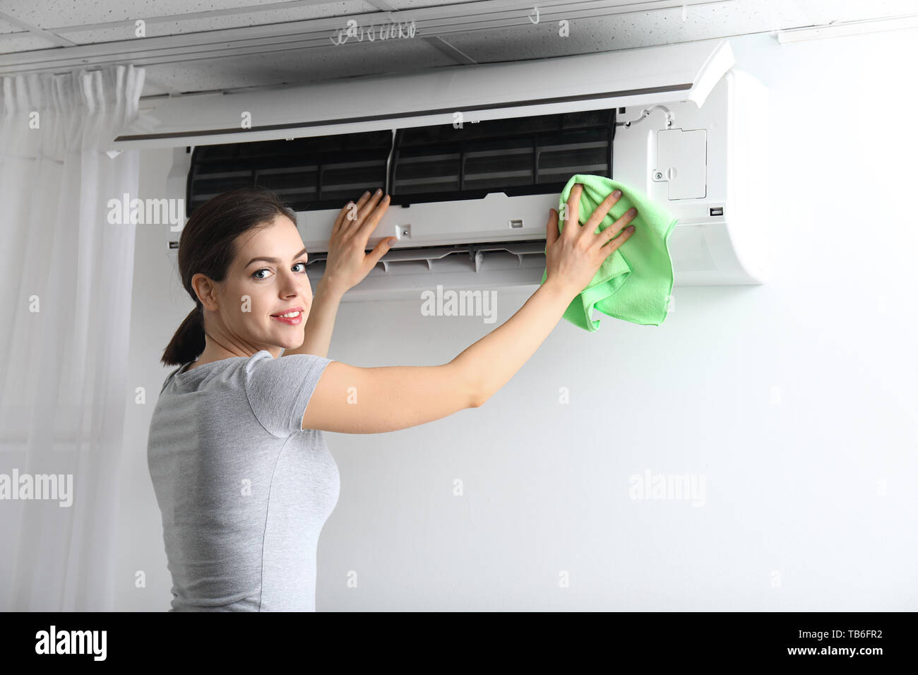 Young woman cleaning air conditioner at home Stock Photo