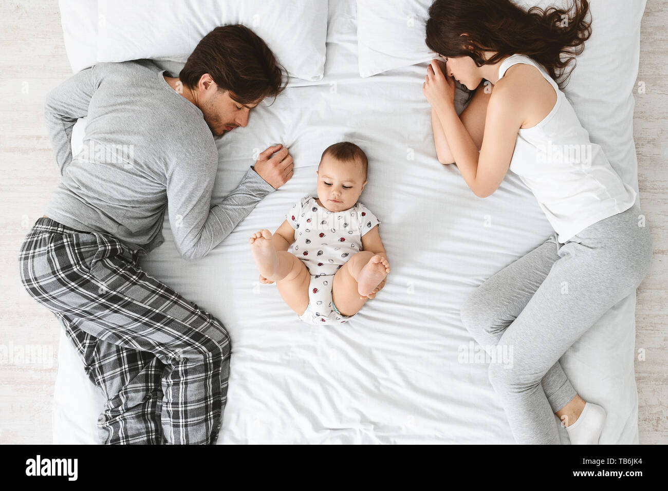 Morning after night. Tired parents sleeping on bed sides adorable baby playing in the middle top view Stock Photo Alamy