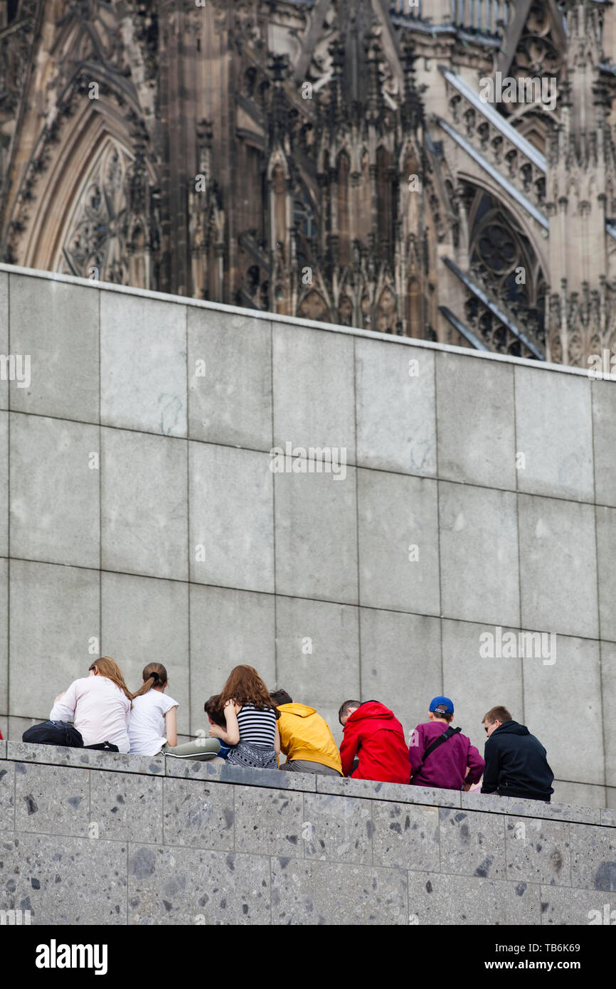 young people sitting on a wall at the Roman-Germanic Museum, the cathedral, Cologne, Germany.  Jugendliche sitzen auf einer Mauer am Roemisch-Germanis Stock Photo