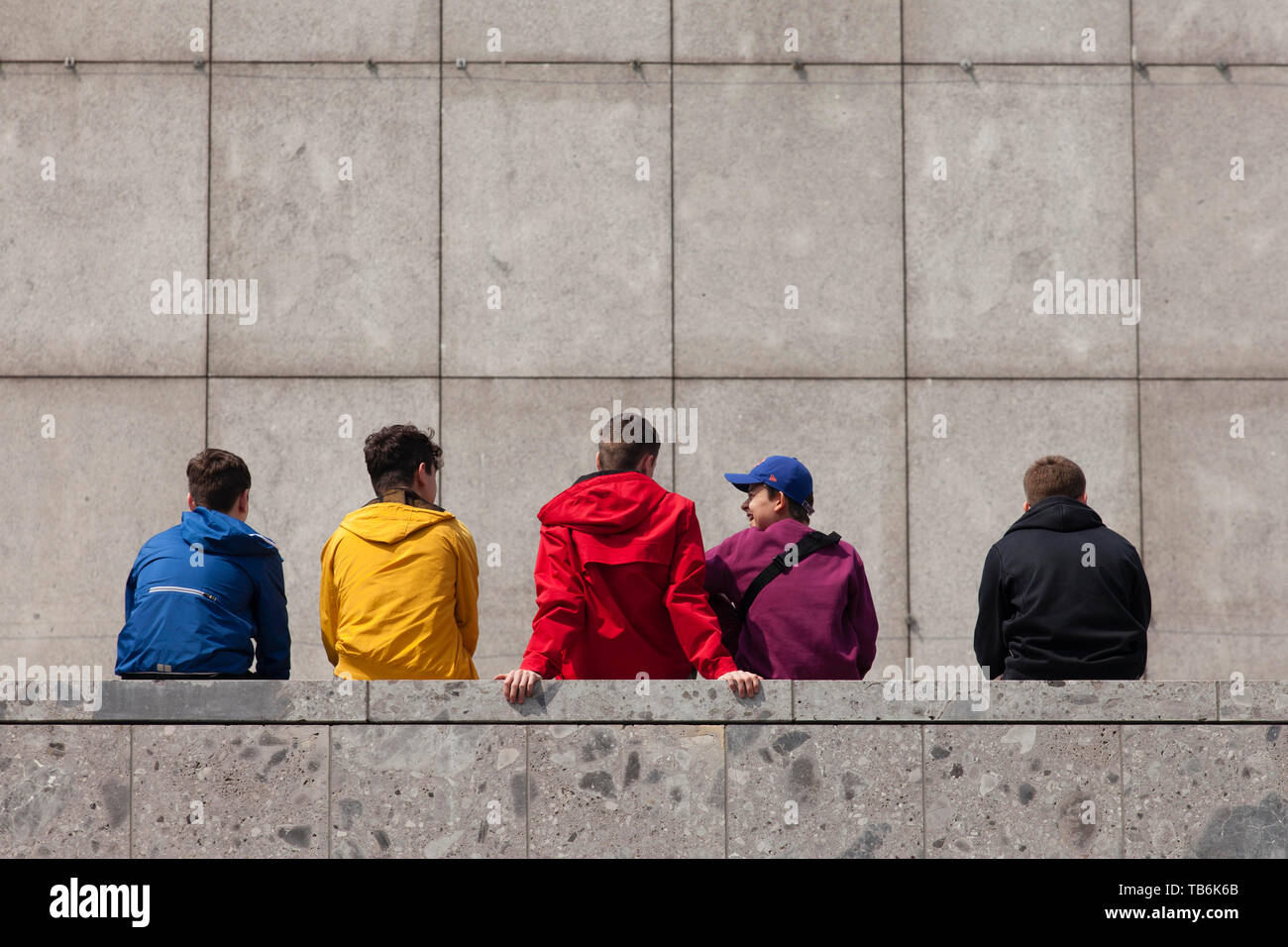 young people sitting on a wall at the Roman-Germanic Museum, Cologne, Germany.  Jugendliche sitzen auf einer Mauer am Roemisch-Germanischen Museum, Ko Stock Photo