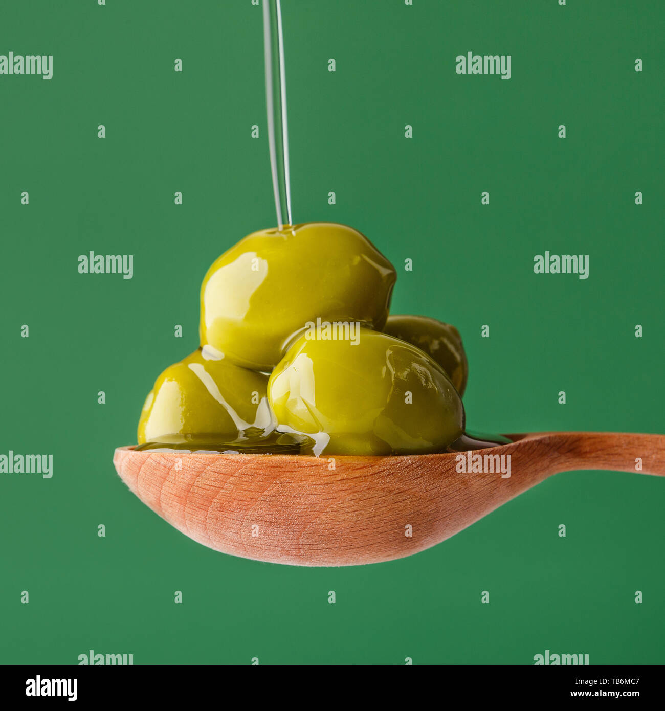 Green olives in wooden spoon and pouring oil on green background Stock ...