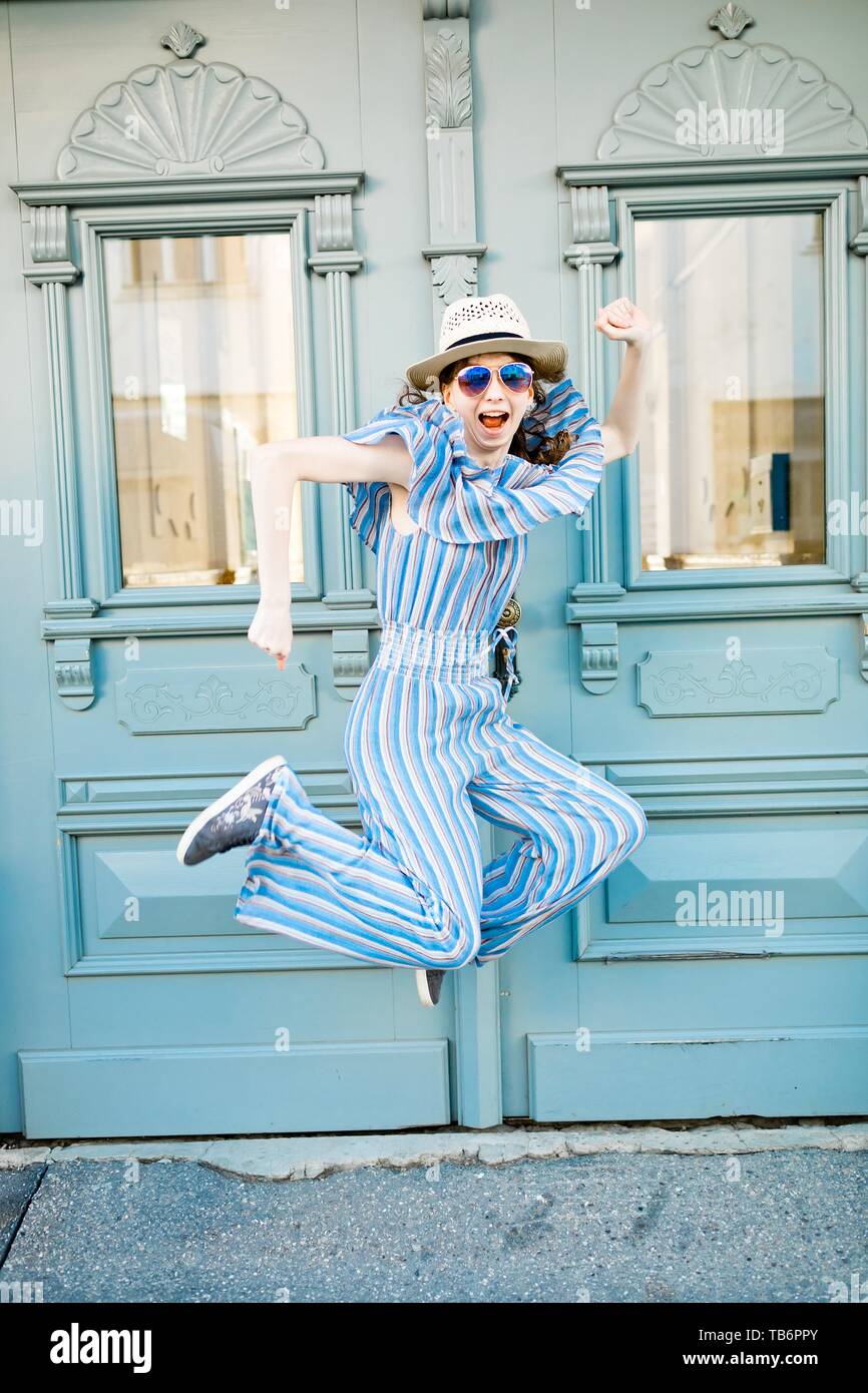 Young girl in jumpsuit is jumping at vintage gate with light blue pastel color Stock Photo