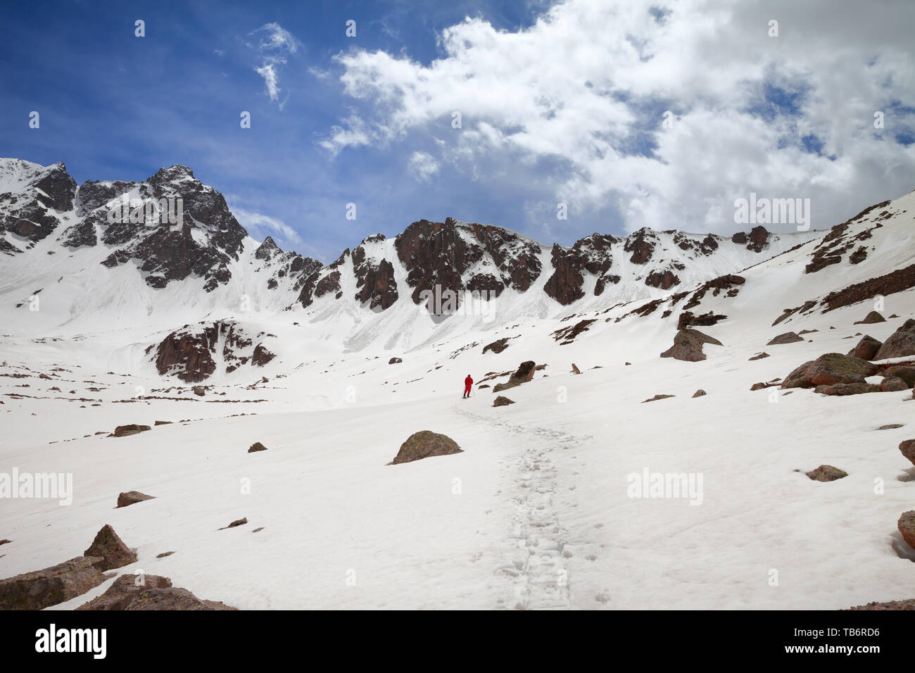 Silhouette of hiker in red on snowy plateau in high mountains at sunny day. Turkey, Kachkar Mountains, highest part of Pontic Mountains. Wide angle vi Stock Photo