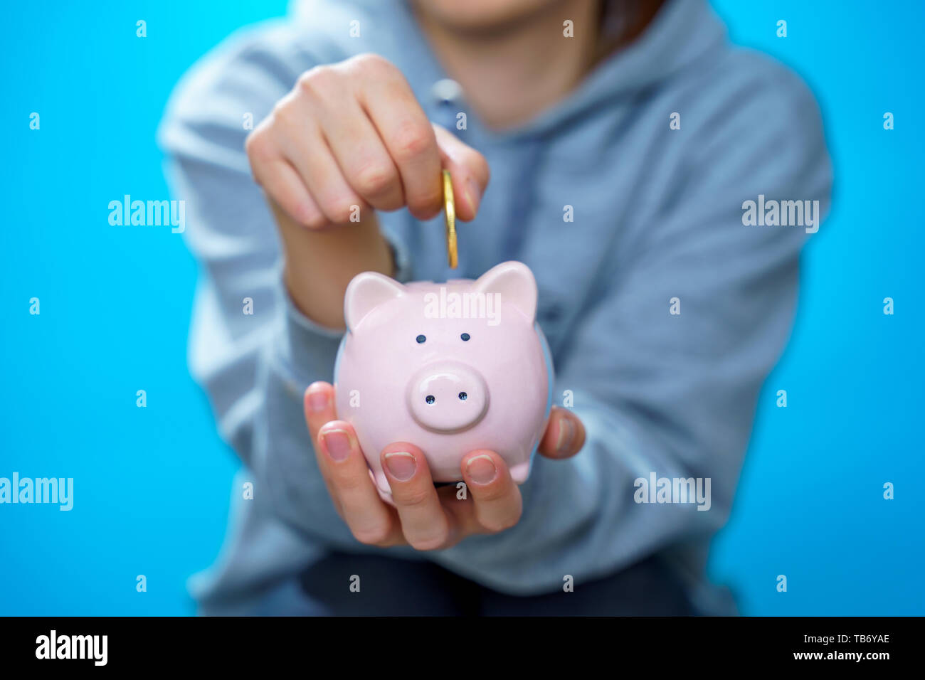 Photo of male throwing coin into piggy bank on blue empty background ...