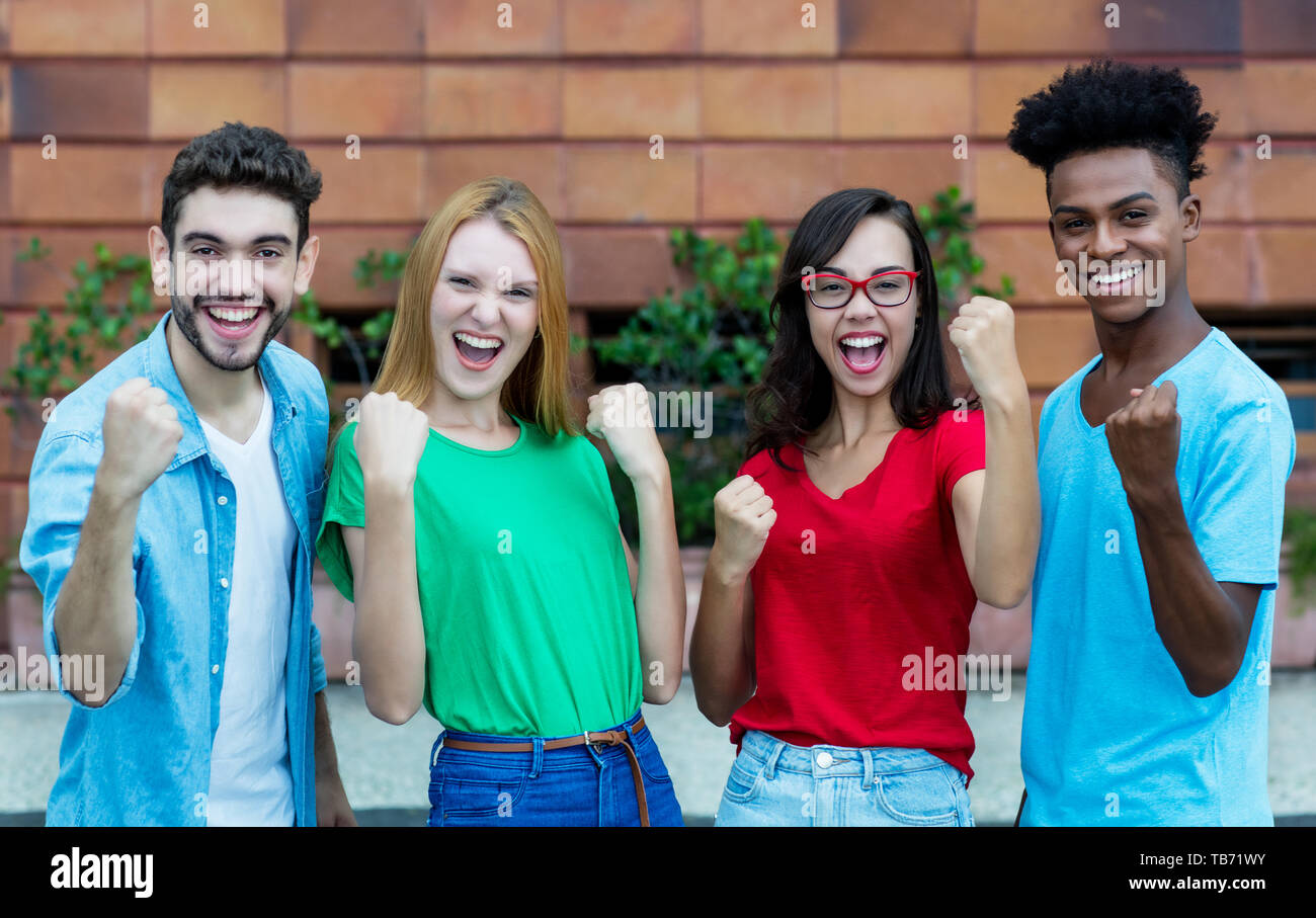 Cheering group of four young adults of generation y showing thumbs outdoor in the summer in the city Stock Photo