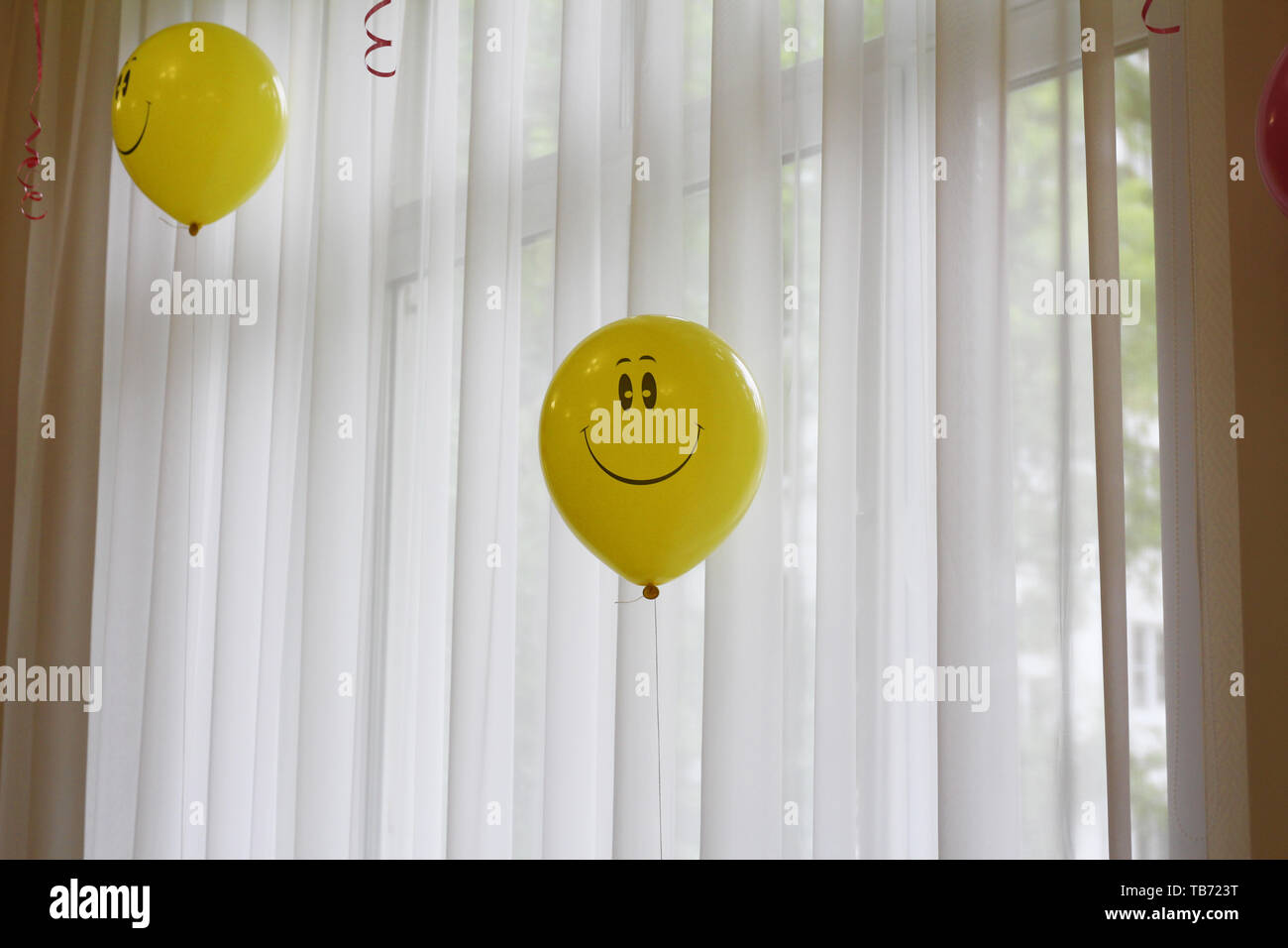 Yellow balloon with a smile. Smiley - a symbol of happiness and joy. Inflatable ball on the background of the window. Stock Photo