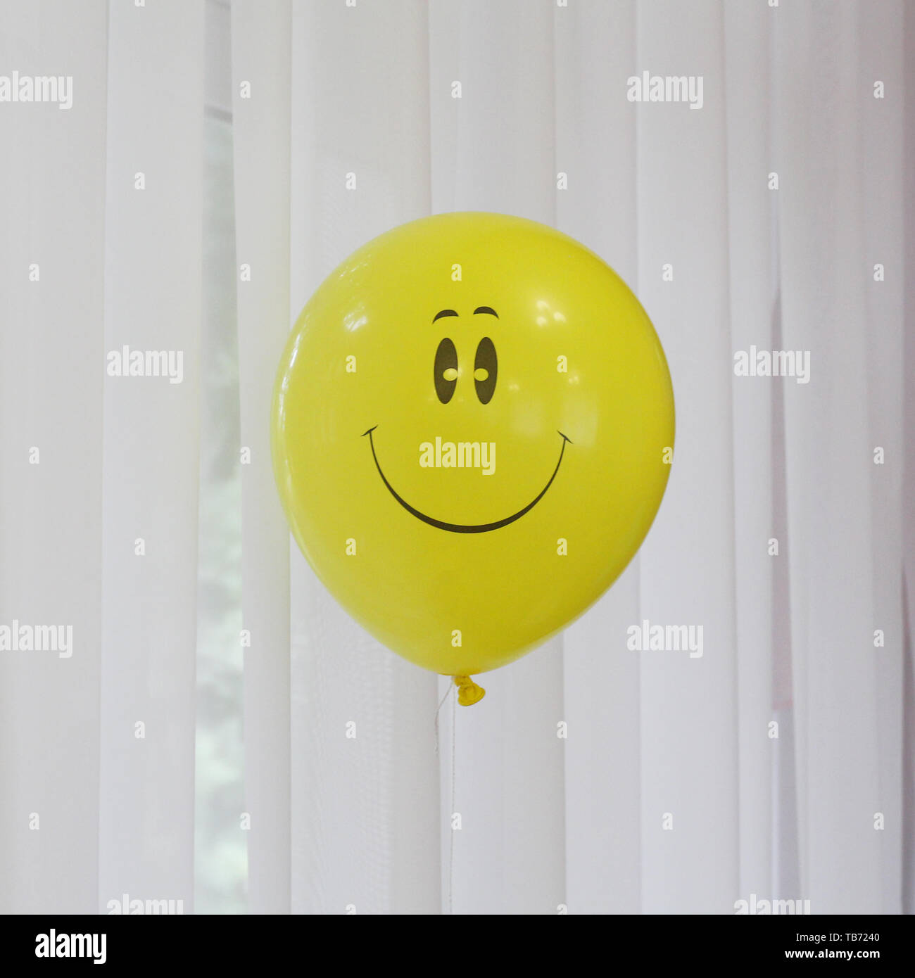 Yellow balloon with a smile. Smiley - a symbol of happiness and joy. Inflatable ball on the background of the window. Stock Photo