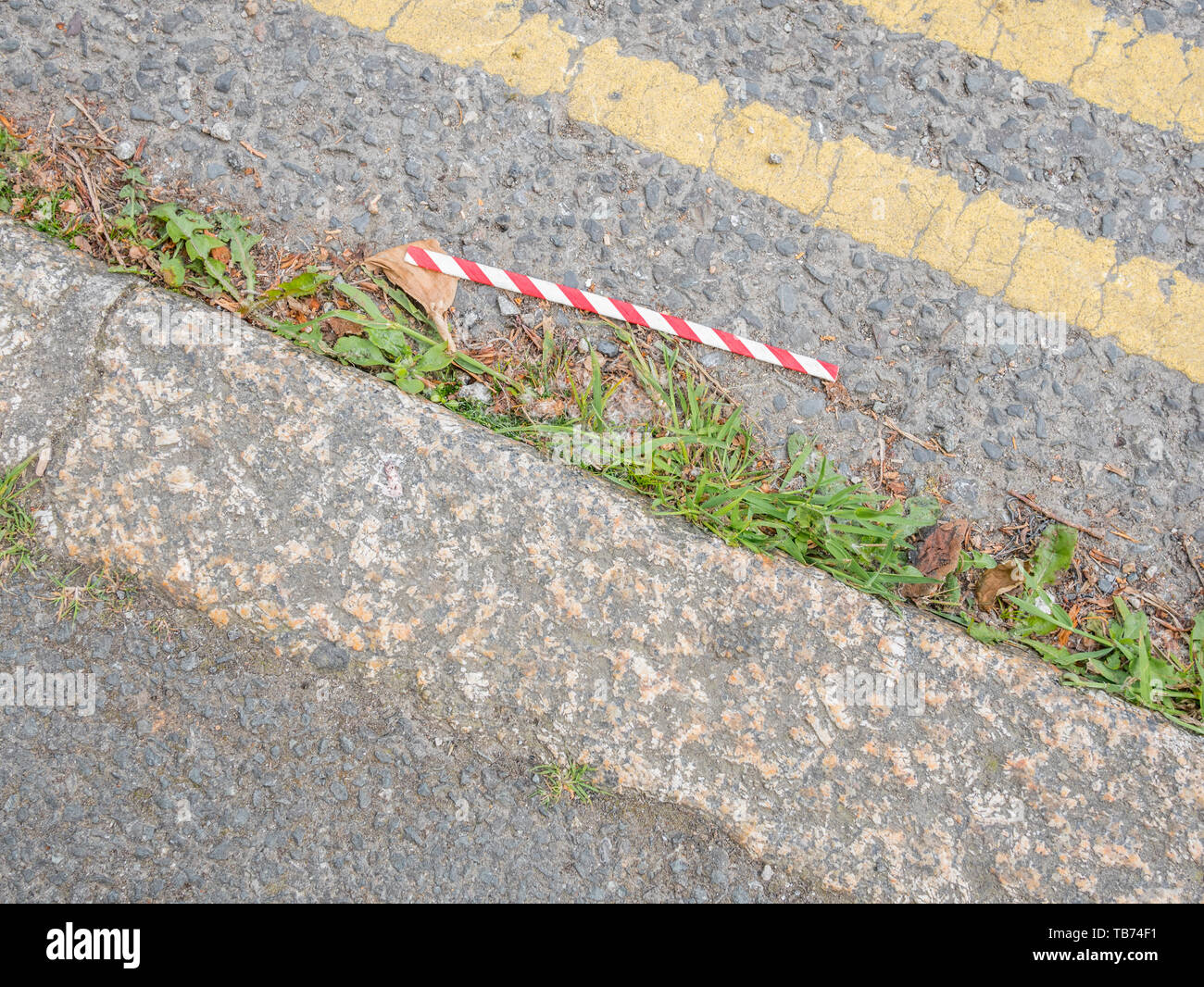 Discarded paper straw littering urban road curbside. Paper straw litter replacing plastic straw litter as the new urban rubbish problem. Stock Photo