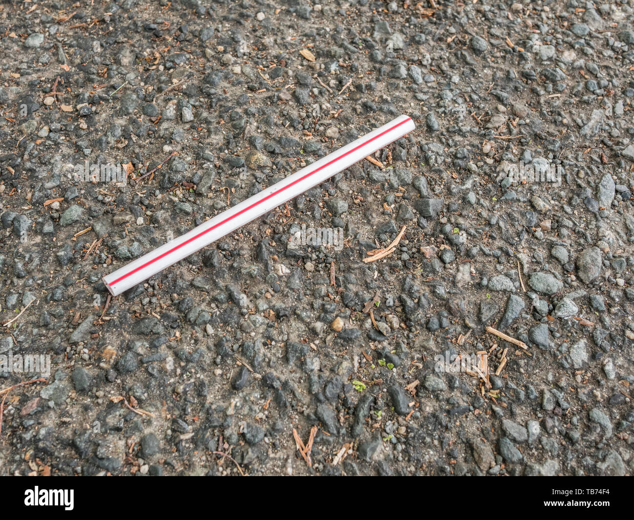 Plastic drinking straw discarded on tarmac road surface in urban area Metaphor plastic straw pollution, environmental pollution, plastic straw ban. Stock Photo