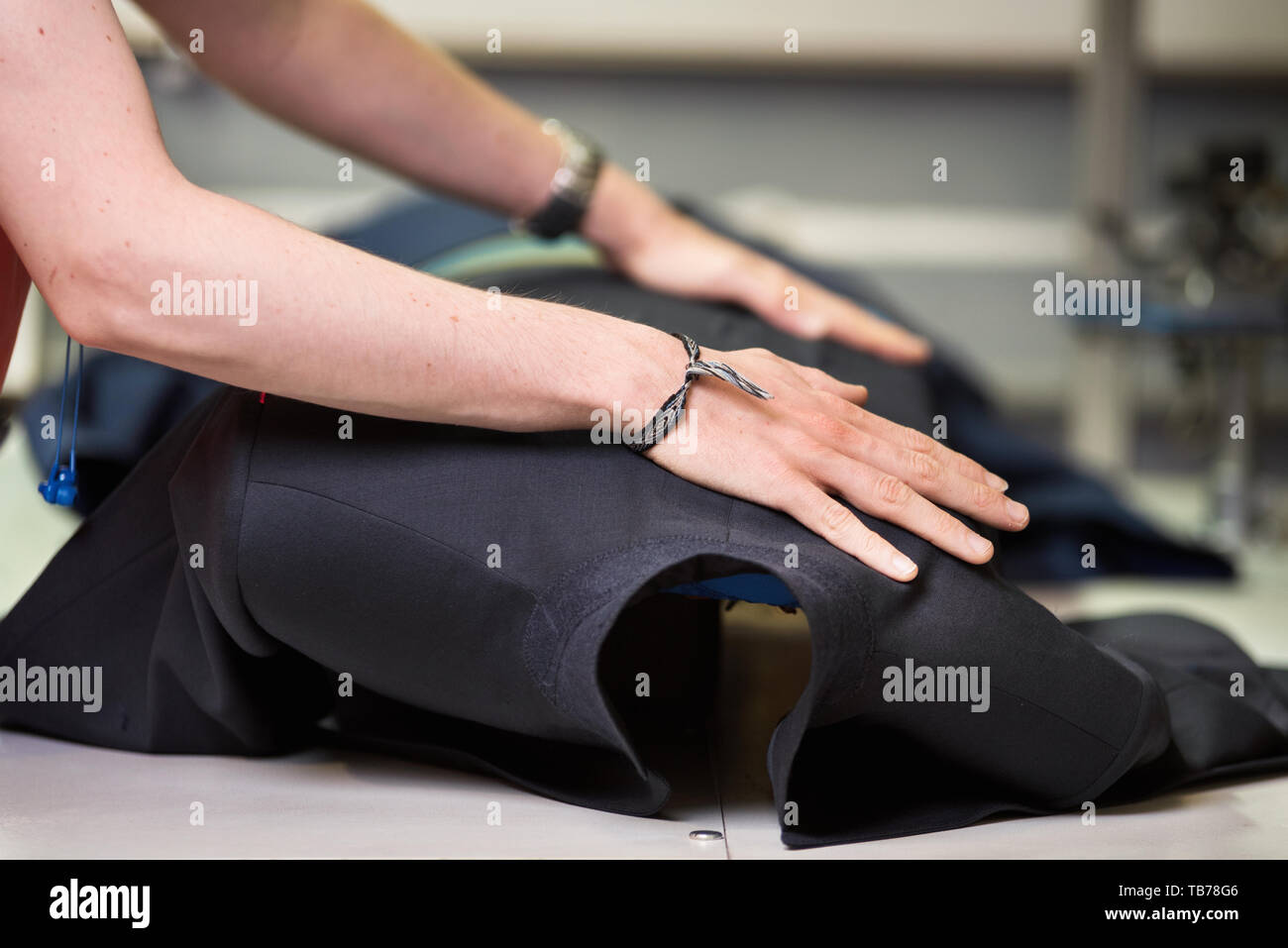 Ironing table. Industrial Presser in sewing suit clothes pressed . Stock Photo