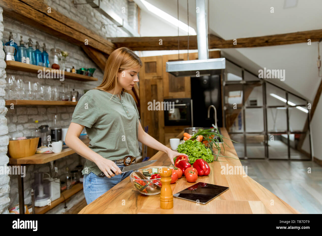 Young woman preparing food in the rustic kitchen while using digital tablet Stock Photo