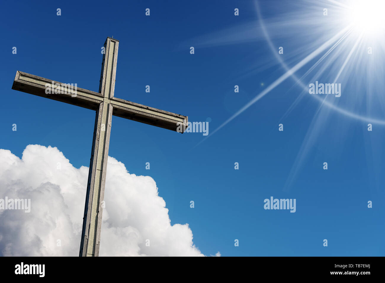 Wooden Christian cross on blue sky with clouds and sun rays - Religious Symbol Stock Photo