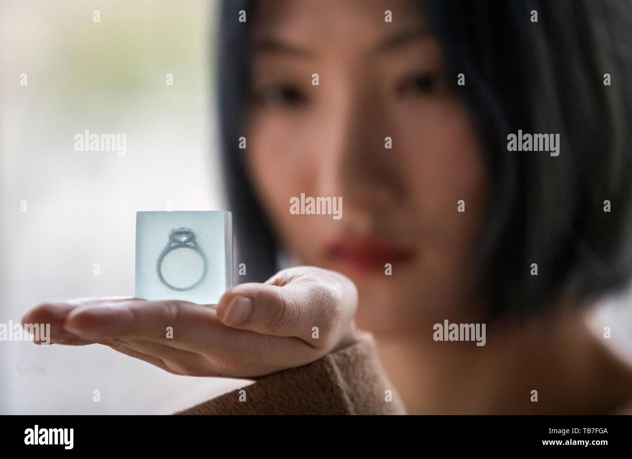 Jewellery design student Zhan Shi takes a closer look at her piece titled Gin on Ice which features a Tiffany ring set inside a glass cube at the media preview of the Edinburgh College of Art degree show in Edinburgh. Stock Photo
