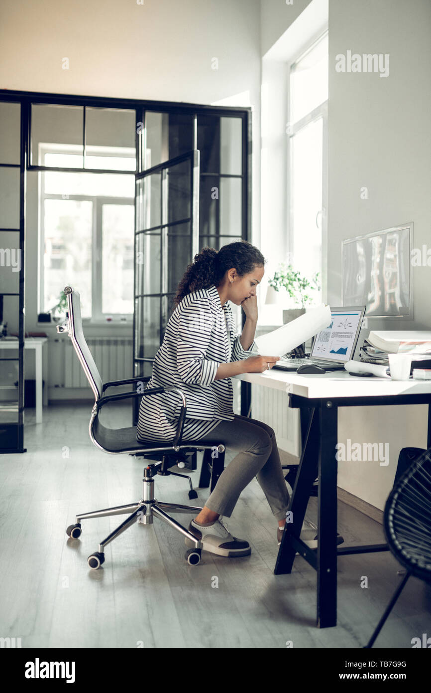 Curly dark-haired trainee feeling overloaded with too many tasks Stock Photo