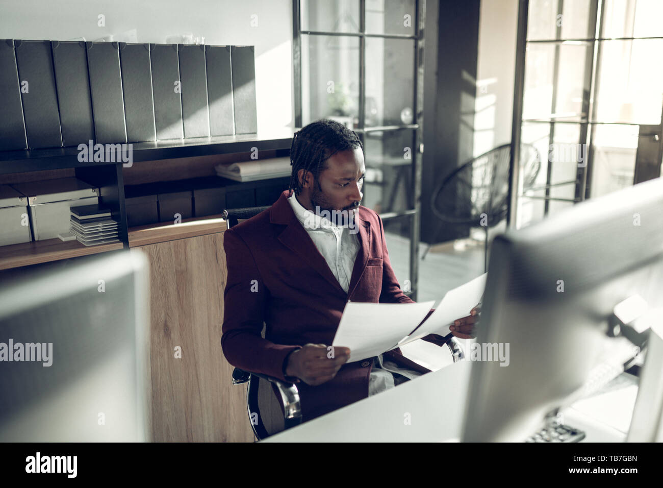 Bearded dark-skinned businessman reading documents in office Stock Photo