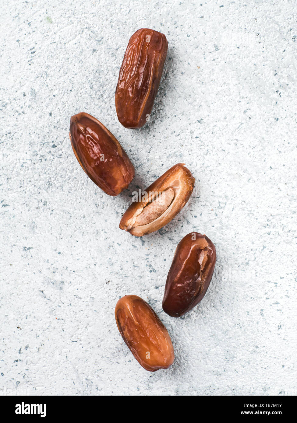 Sweet raw dates on gray cement background. Whole dates and half with bone date on grey concrete surface. Sugar free alternatives concept with space for text. Top view or flat-lay. Vertical. Stock Photo