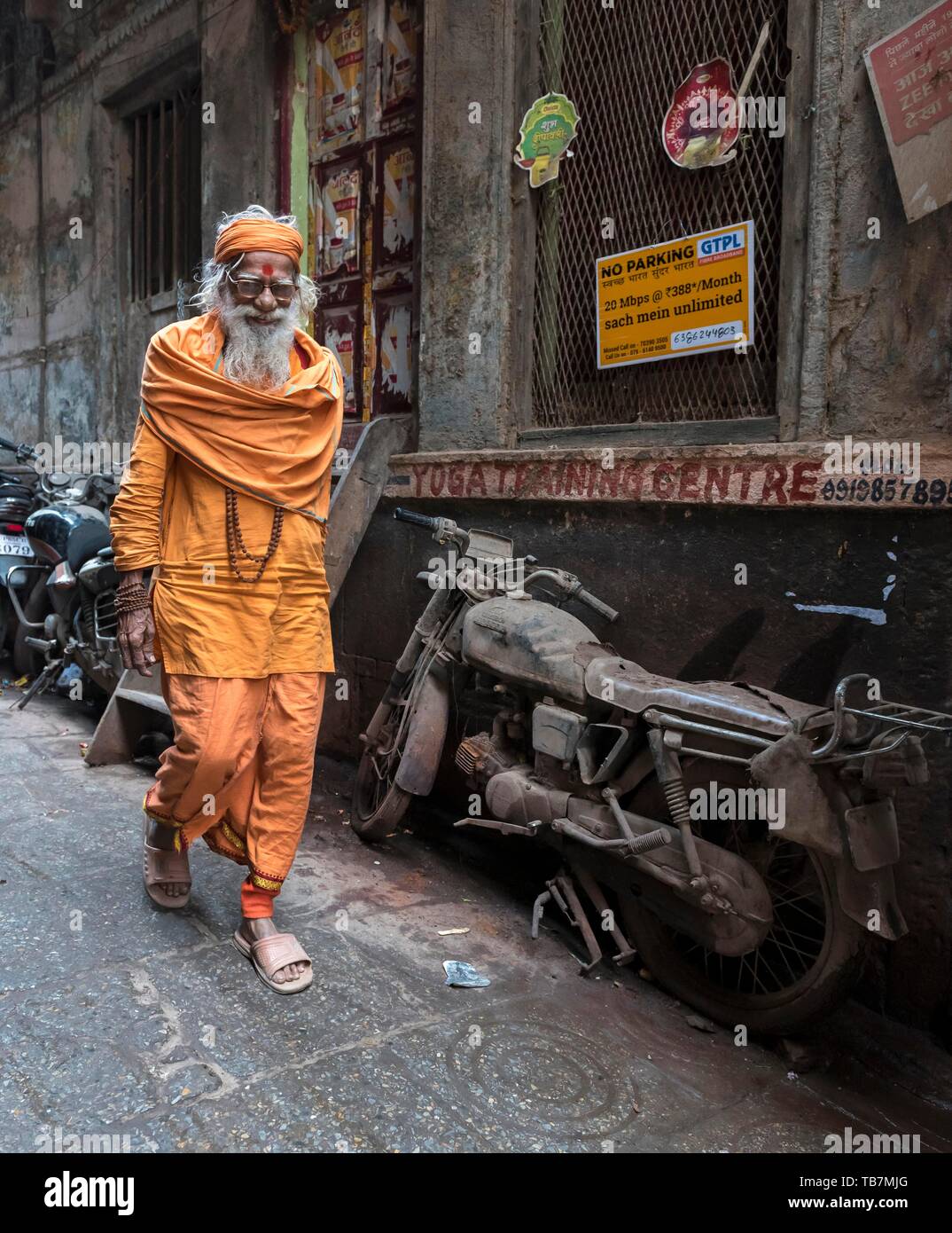 Hindu priest walks pass an abandoned motorcycle in the narrow streets, Old City of Varanasi, Uttar Pradesh, India Stock Photo