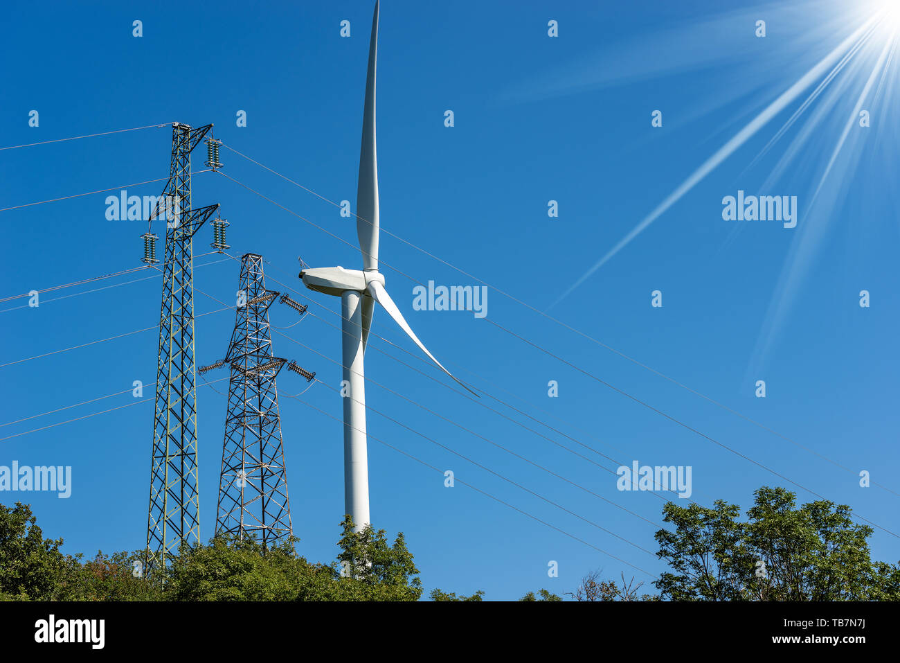 Wind turbine and high voltage towers (power line) on a clear blue sky with sun rays - Renewable energy concept Stock Photo
