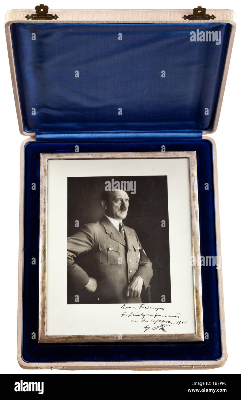 Roman Feldmeyer (1895 - 1950) - a Führer portrait in a silver presentation frame, Hoffmann half-length portrait of Adolf Hitler in Party uniform. Hand-written dedication in ink (tr.) 'Roman Feldmeyer in remembrance of the 12/October 1940 - Adolf Hitler'. Under glass, in a silver frame, at bottom fineness mark crown/'835', the back with support stand (securing strap loosely included). Dimensions 29.5 x 23.5 cm. In a presentation case covered in light-brown cloth, dark-blue velvet insert and silk cover lining. Signs of age, the cloth covering on the lower edge of the case loo, Editorial-Use-Only Stock Photo