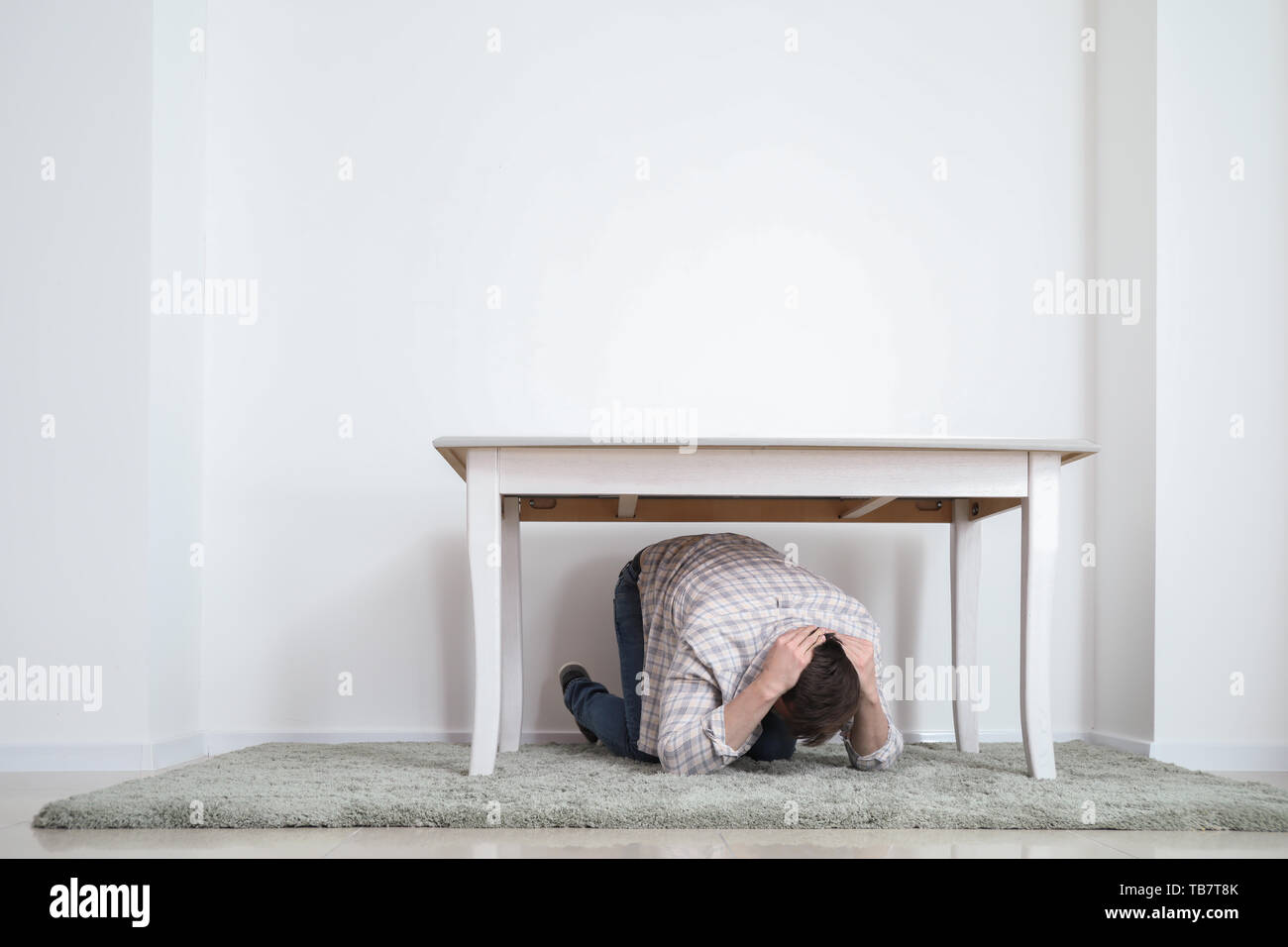 Young man under table during earthquake indoors Stock Photo