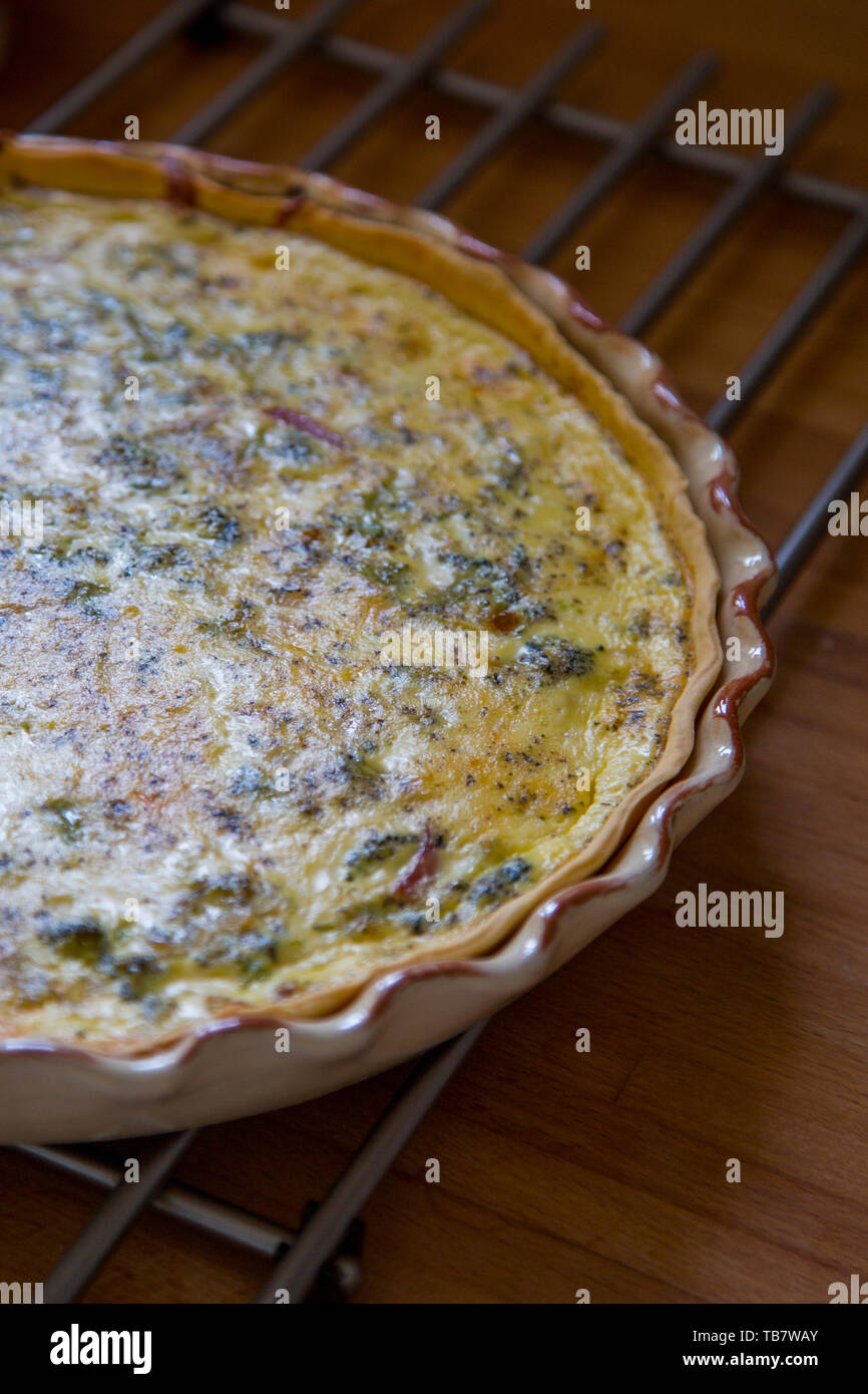 Closeup on vegetable quiche in ceramic baking dish on cooling rach on wooden countertop. Stock Photo