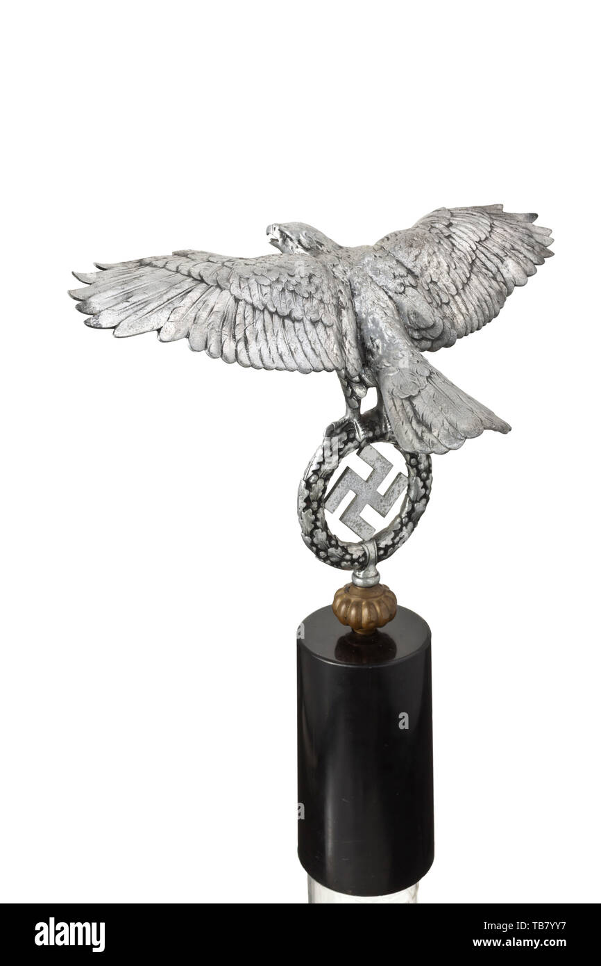A large eagle for a Jingling Johnny, Wrought of polished aluminium. The eagle in relief with outspread wings, clutching the oak leaf wreath with a swastika in its talons. A flattened ball in non-ferrous metal screwed onto the bottom (part of the Jingling Johnny). On a matching black stone pedestal. A crack at the base of the left wing, showing signs of age. Wingspan ca. 55 cm, height without pedestal ca. 35 cm, total height ca. 56 cm. The large version of an extremely rare part of Wehrmacht equipment. historic, historical 20th century, Editorial-Use-Only Stock Photo