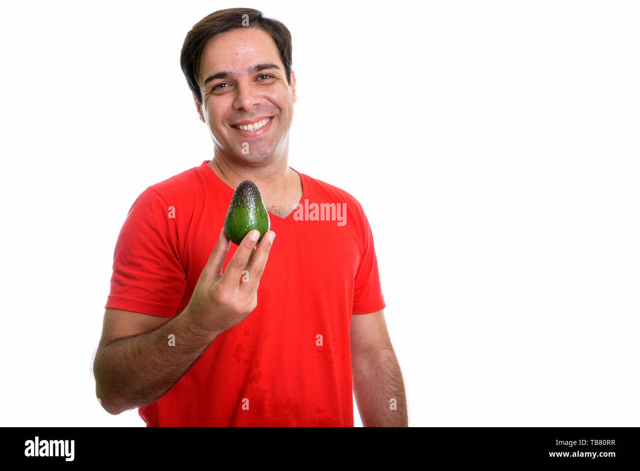 Studio shot of young happy Persian man smiling while holding avocado ...