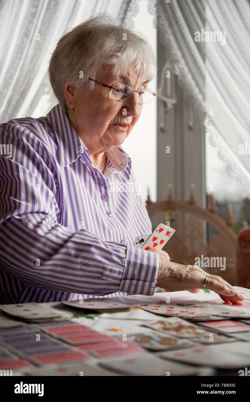 Very old senior lady playing cards alone at home Stock Photo