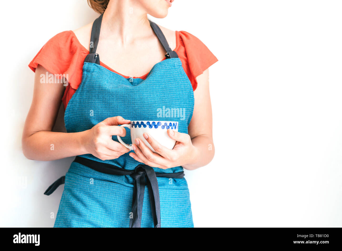 Woman in casual stylish clothes, pink dress and blue apron with a big cup of coffee in her hands on an isolated white background, morning for a housew Stock Photo