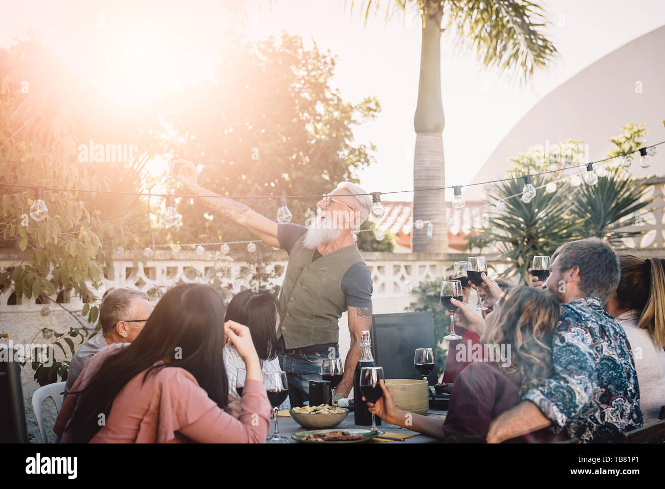 Happy family taking selfie with mobile smartphone camera at dinner party outdoor - People with different ages and ethnicity eating together on patio Stock Photo