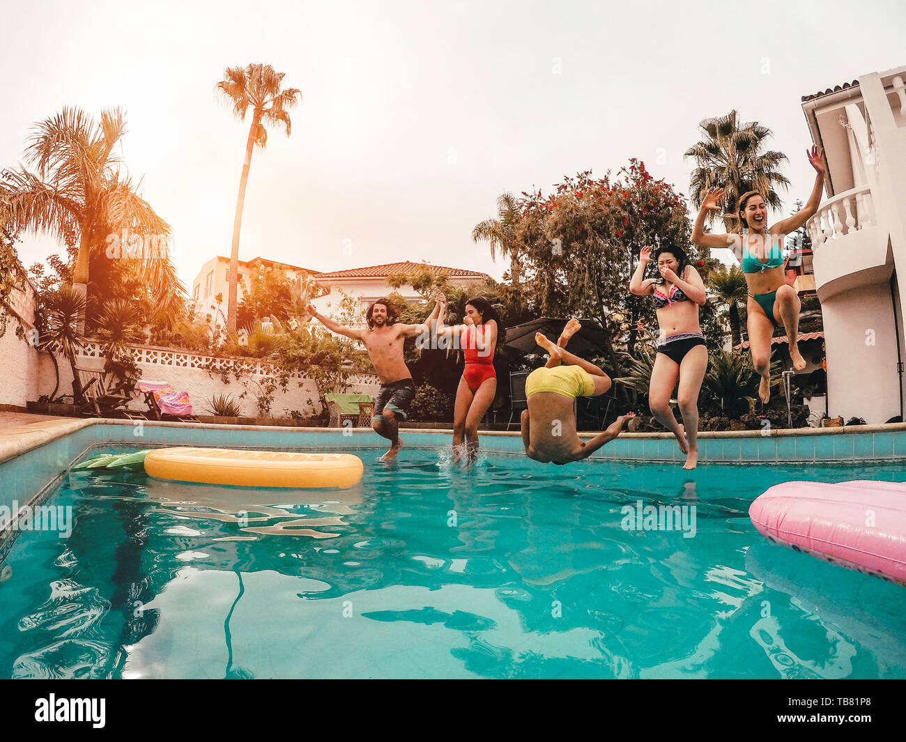 Group of happy friends jumping in pool at sunset time - Crazy young people having fun making party in exclusive tropical house Stock Photo