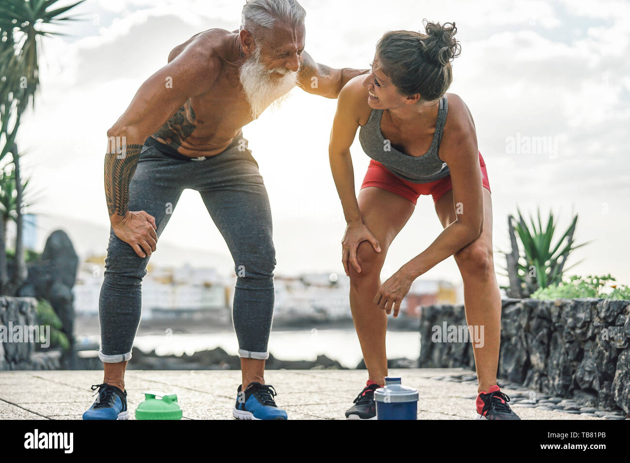 Fit couple having a break after a fast race next the beach at sunset - Sporty people workout running outdoor Stock Photo
