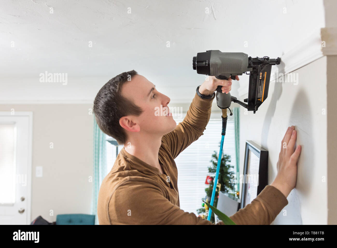 Black and grey air compressed nail gun used to install white wood crown