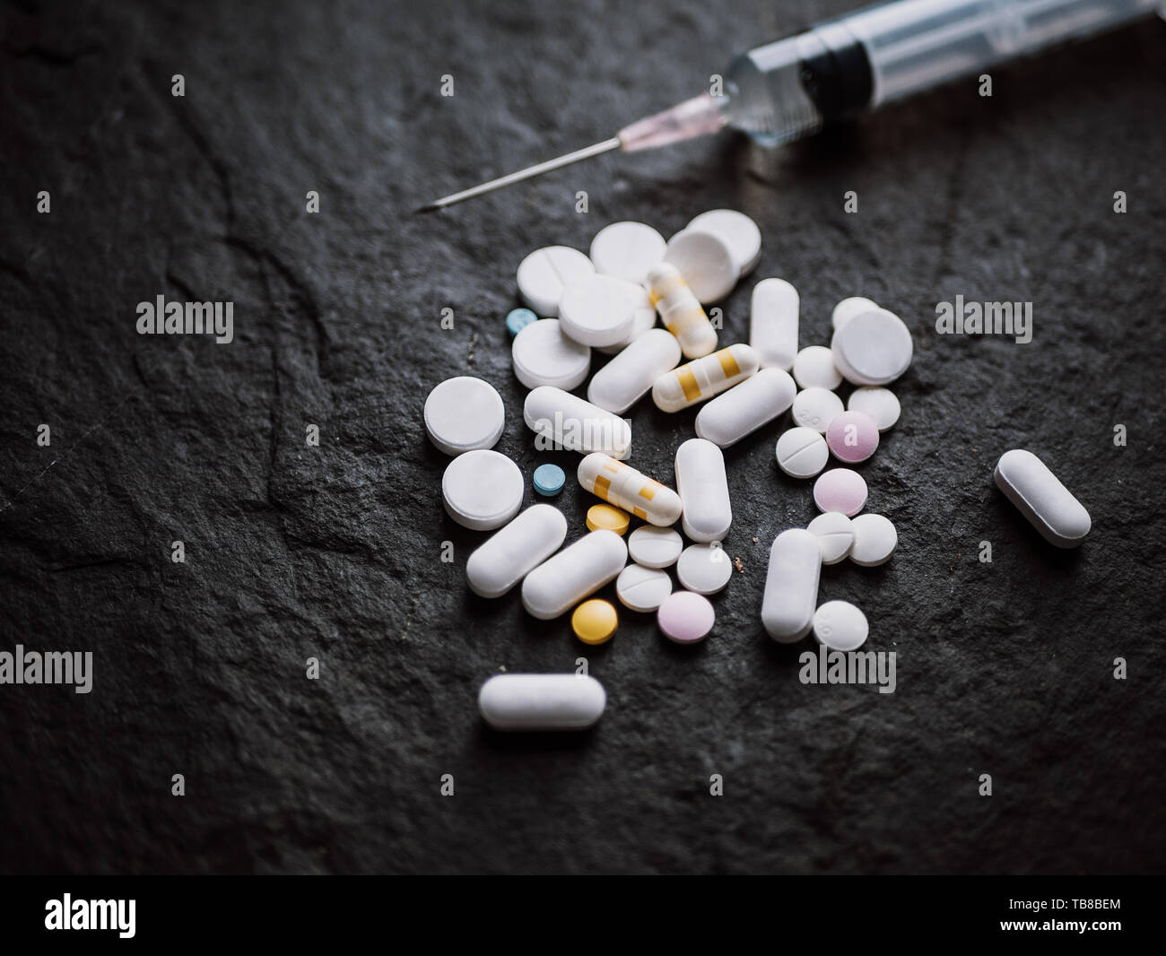 assorted colorful pharmaceutical medicine pills tablets and capsules with hypodermic syringe injection needle on black stone background. pharmacy and  Stock Photo
