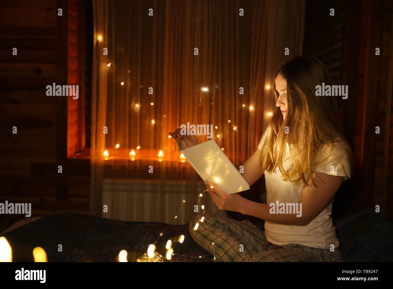 Beautiful woman reading fairy tales in darkness with glowing lights Stock Photo