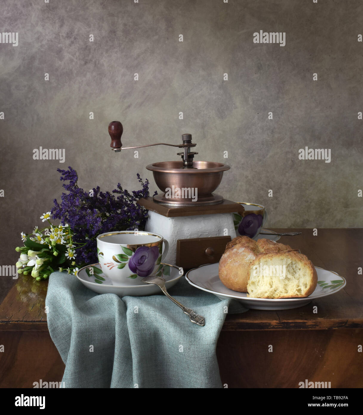 Retro still life poster breakfast. Vintage coffee grinder cups, silver spoon, homemade bread bakery. Dark light, wooden table, linen textile fabric Stock Photo