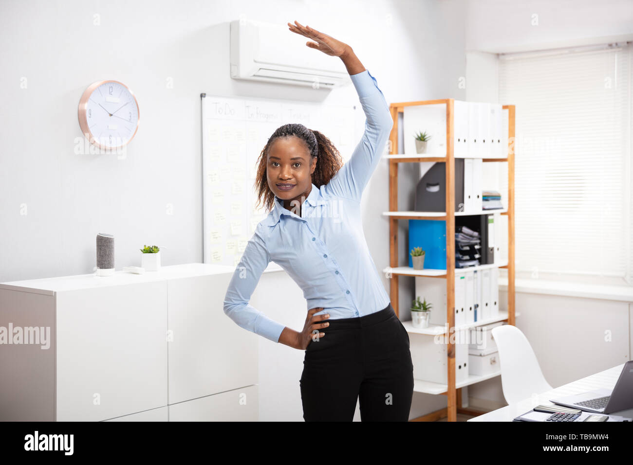 Young Businesswoman Doing Yoga Standing In Front Of Office Desk