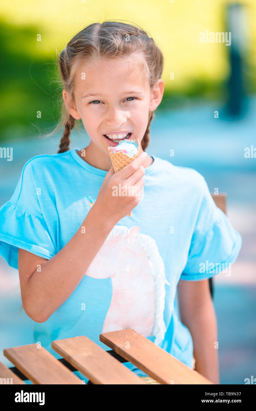 Little girl eating ice-cream at summer in outdoor cafe. Cute kid ...