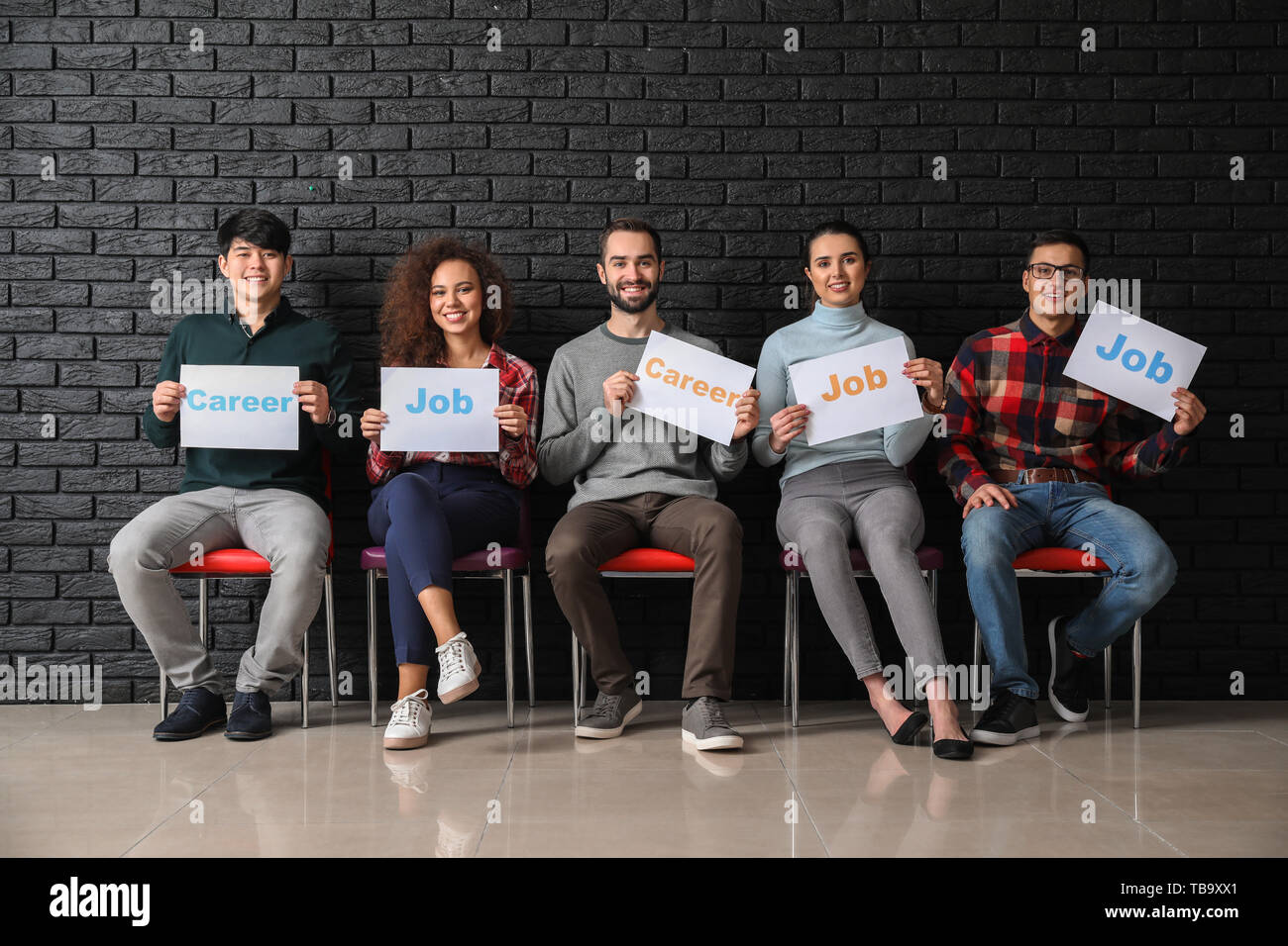 Young people holding paper sheets with words JOB and CAREER indoors