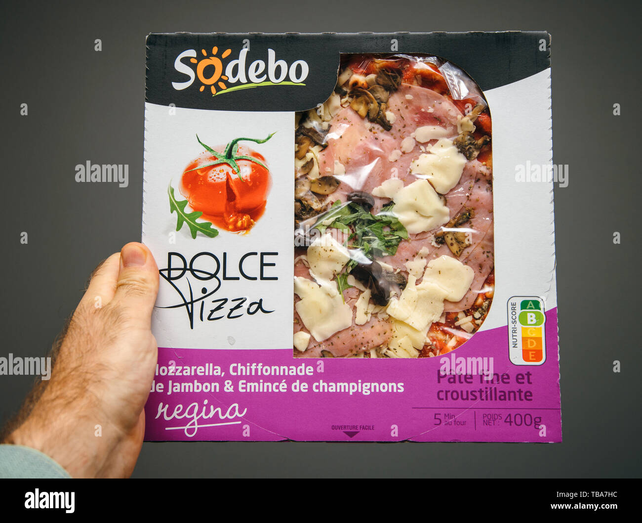 Strasbourg, France - May 27, 2019: Man hand holding against gray background a box with pre-frozen pizza made by French company Sodebo Dolce Pizza REgina Stock Photo