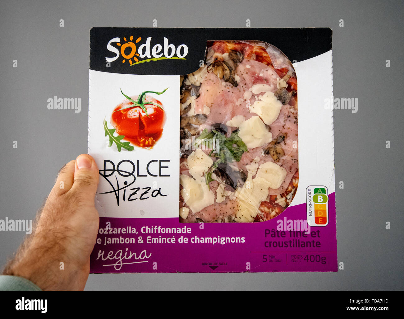Strasbourg, France - May 27, 2019: Man hand holding against gray background a box with pre-frozen pizza made by French company Sodebo Dolce Pizza REgina Stock Photo